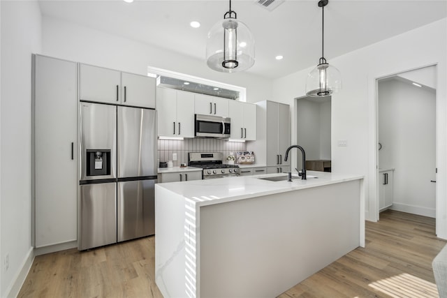 kitchen featuring sink, light hardwood / wood-style flooring, decorative light fixtures, and appliances with stainless steel finishes