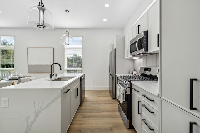 kitchen with stainless steel appliances, sink, light hardwood / wood-style flooring, white cabinets, and hanging light fixtures