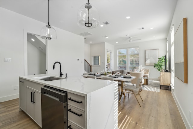 kitchen featuring dishwasher, a kitchen island with sink, white cabinets, hanging light fixtures, and light wood-type flooring