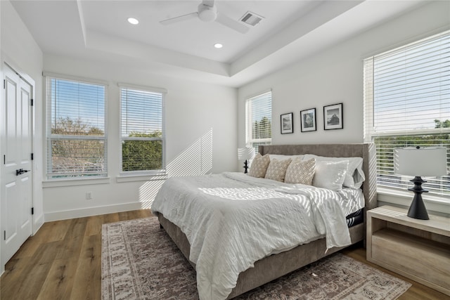 bedroom featuring ceiling fan, a raised ceiling, dark wood-type flooring, and multiple windows