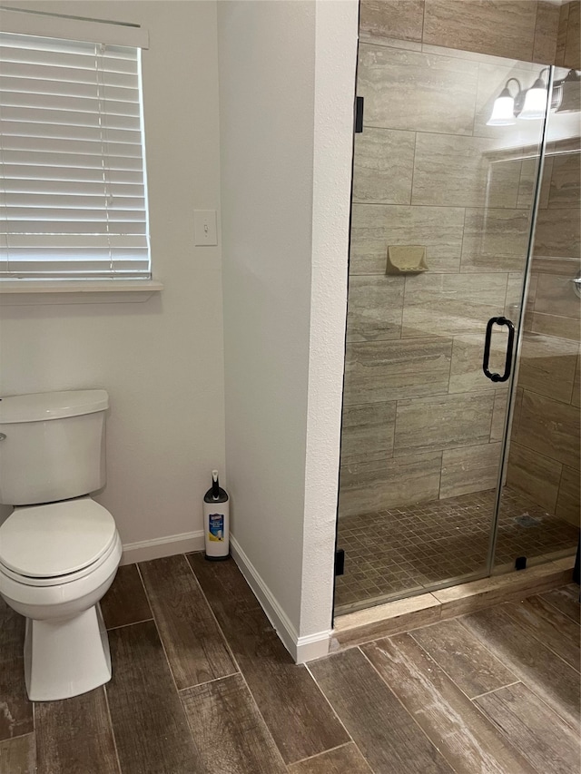 bathroom with wood-type flooring, a shower with shower door, and toilet