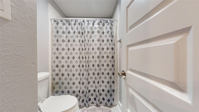 bathroom with a textured wall, a shower with shower curtain, and toilet