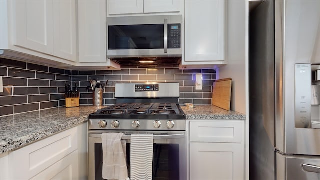 kitchen featuring stainless steel appliances, white cabinets, decorative backsplash, and light stone countertops