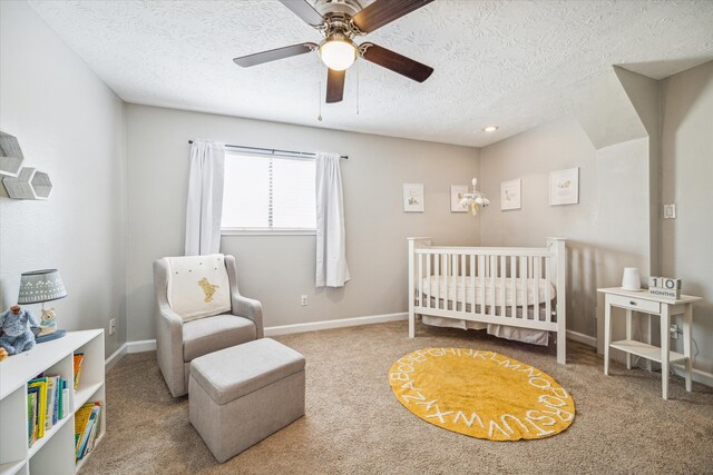 bedroom featuring a nursery area, carpet, a textured ceiling, and ceiling fan