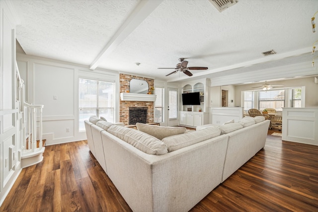 living room with built in shelves, a textured ceiling, dark hardwood / wood-style floors, beamed ceiling, and a fireplace