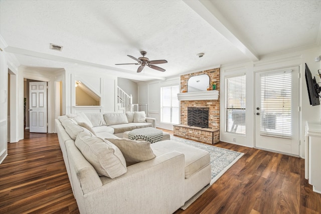 living room featuring dark wood-type flooring, ceiling fan, a fireplace, a textured ceiling, and beamed ceiling