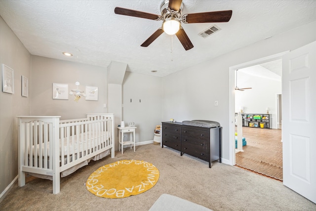 bedroom with ceiling fan, light colored carpet, a textured ceiling, and a crib