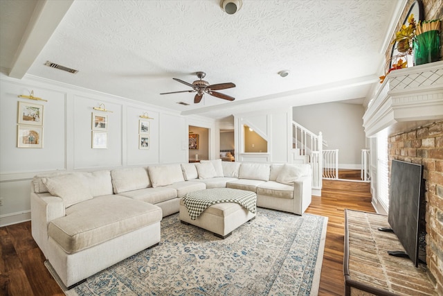 living room with crown molding, ceiling fan, wood-type flooring, a textured ceiling, and a brick fireplace