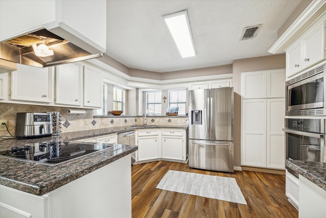 kitchen with range hood, dark stone countertops, white cabinets, stainless steel appliances, and dark wood-type flooring