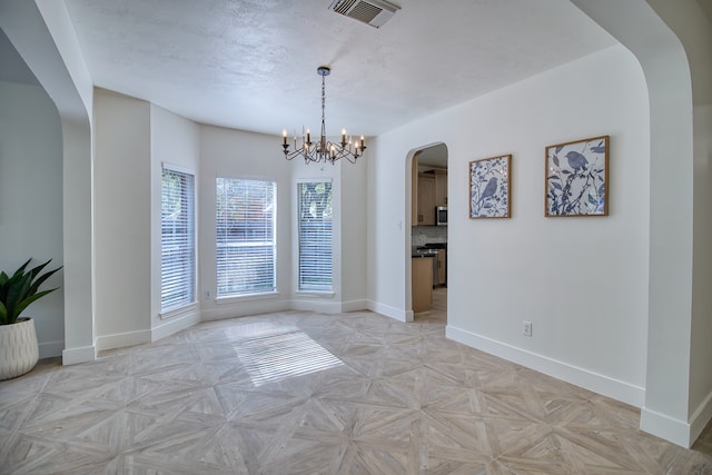 unfurnished dining area featuring a notable chandelier, a textured ceiling, and light parquet flooring