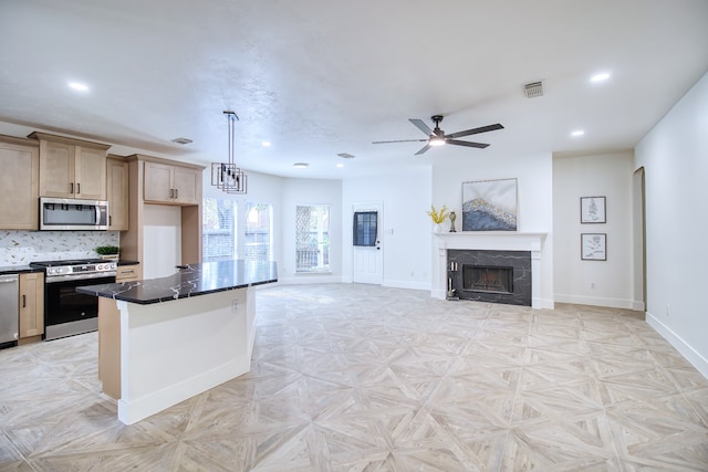 kitchen featuring a center island, a tile fireplace, hanging light fixtures, ceiling fan, and stainless steel appliances