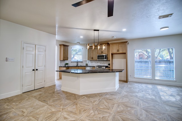 kitchen with a center island, hanging light fixtures, ceiling fan, decorative backsplash, and stainless steel appliances