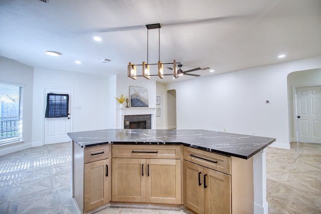 kitchen with ceiling fan with notable chandelier, a kitchen island, hanging light fixtures, and dark stone counters