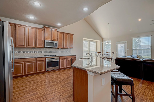 kitchen featuring stainless steel appliances, vaulted ceiling, decorative light fixtures, a center island with sink, and a breakfast bar area