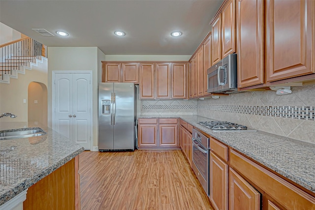 kitchen with light stone countertops, sink, tasteful backsplash, light hardwood / wood-style floors, and appliances with stainless steel finishes