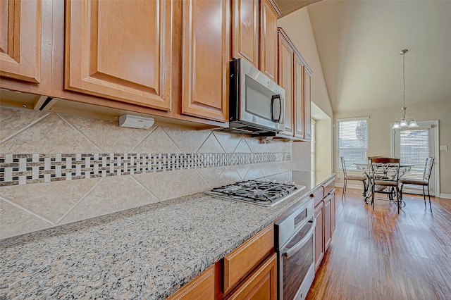 kitchen featuring lofted ceiling, decorative backsplash, light stone counters, stainless steel appliances, and a chandelier