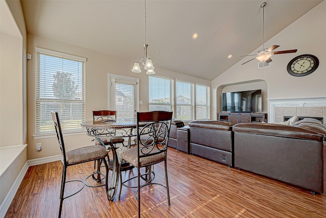 dining area with ceiling fan with notable chandelier, a healthy amount of sunlight, light wood-type flooring, and a fireplace