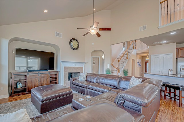 living room featuring a tile fireplace, ceiling fan, sink, light hardwood / wood-style flooring, and high vaulted ceiling