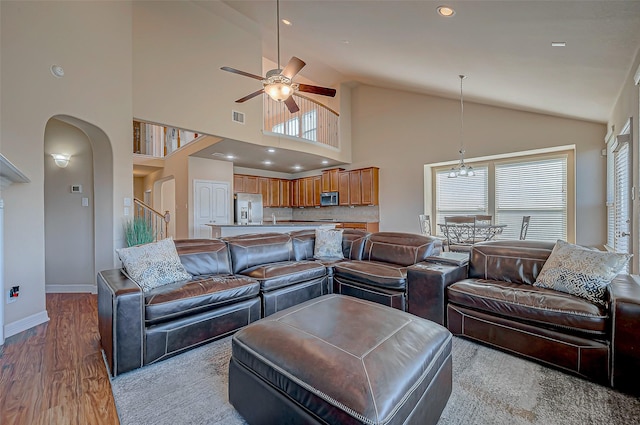 living room featuring ceiling fan with notable chandelier, light wood-type flooring, and high vaulted ceiling