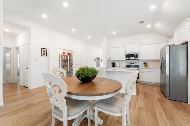 dining space featuring sink, light hardwood / wood-style floors, and vaulted ceiling