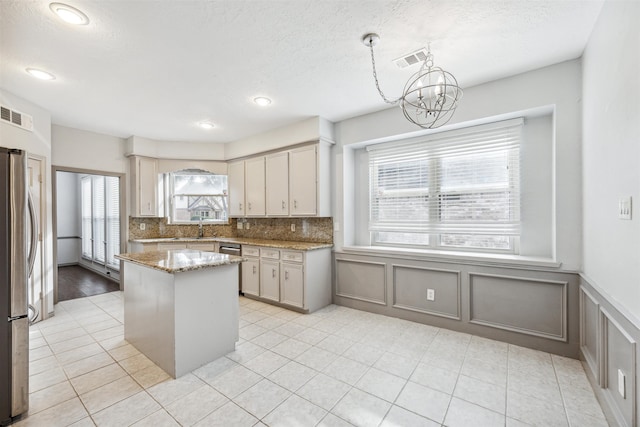 kitchen featuring stainless steel refrigerator, light stone countertops, an inviting chandelier, backsplash, and decorative light fixtures