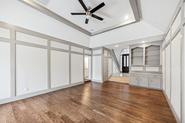 unfurnished living room featuring a raised ceiling, ceiling fan, dark hardwood / wood-style flooring, and a towering ceiling