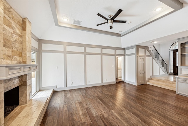 unfurnished living room with ceiling fan, a high ceiling, a raised ceiling, a tiled fireplace, and hardwood / wood-style flooring