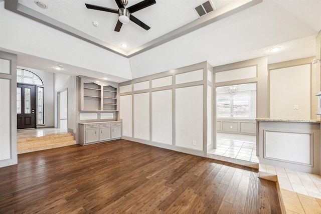 unfurnished living room with built in features, ceiling fan with notable chandelier, and dark hardwood / wood-style floors