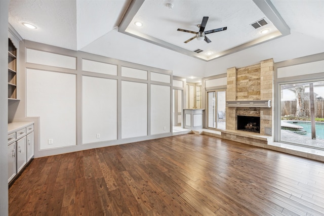 unfurnished living room featuring a tray ceiling, a stone fireplace, hardwood / wood-style flooring, and ceiling fan