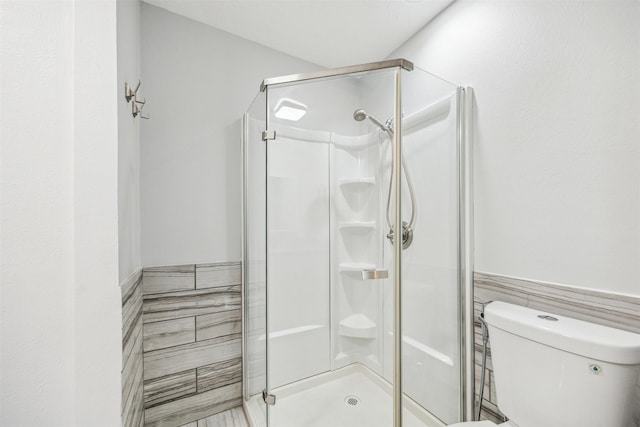 bathroom featuring a shower with shower door, tile walls, and toilet