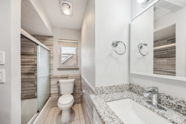 full bathroom featuring vanity, toilet, tile walls, and enclosed tub / shower combo