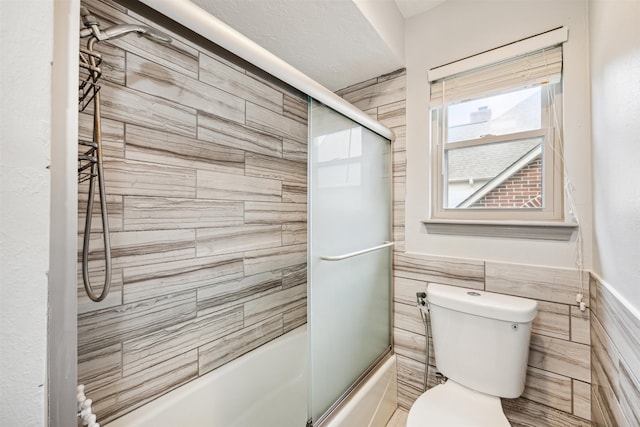 bathroom with toilet, tile walls, and enclosed tub / shower combo