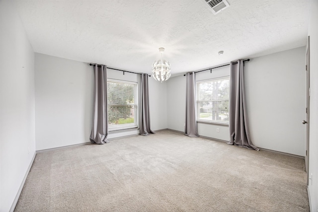 carpeted empty room with a textured ceiling, a wealth of natural light, and an inviting chandelier