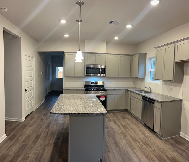 kitchen with appliances with stainless steel finishes, gray cabinetry, hanging light fixtures, light stone counters, and a kitchen island