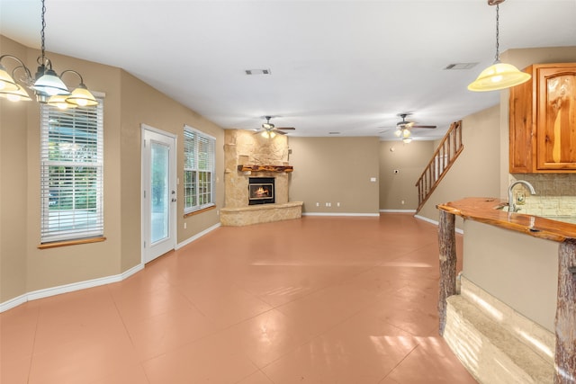 unfurnished living room featuring light tile patterned floors, ceiling fan with notable chandelier, a stone fireplace, and sink