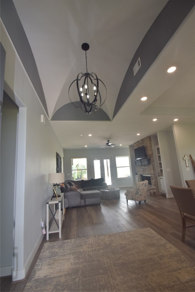 living room featuring dark hardwood / wood-style floors, a fireplace, ceiling fan with notable chandelier, and vaulted ceiling