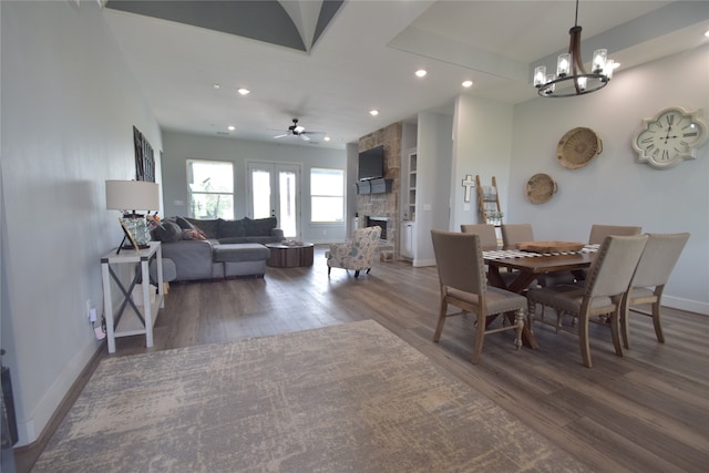 dining room with ceiling fan with notable chandelier, dark hardwood / wood-style floors, and a stone fireplace