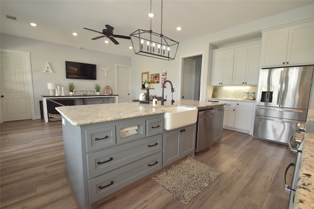 kitchen featuring white cabinets, sink, stainless steel appliances, and an island with sink