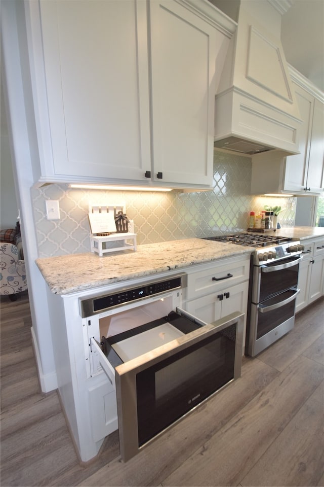 kitchen featuring decorative backsplash, light stone countertops, light hardwood / wood-style flooring, double oven range, and white cabinetry