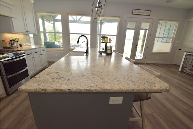 kitchen with a kitchen island with sink, dark wood-type flooring, sink, decorative light fixtures, and stainless steel range oven