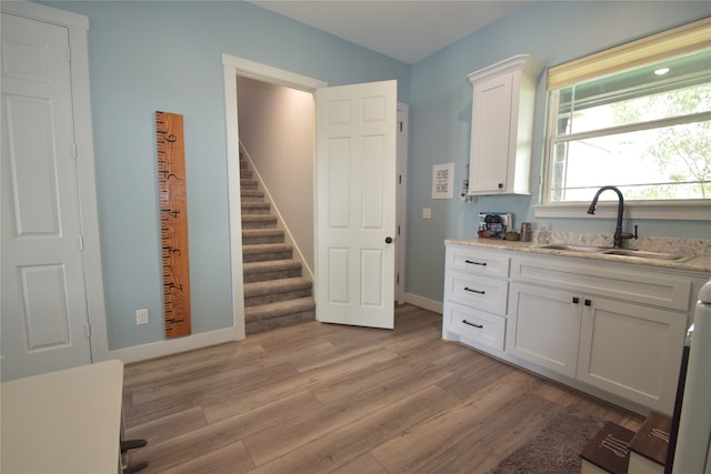 kitchen with light stone countertops, light wood-type flooring, white cabinetry, and sink