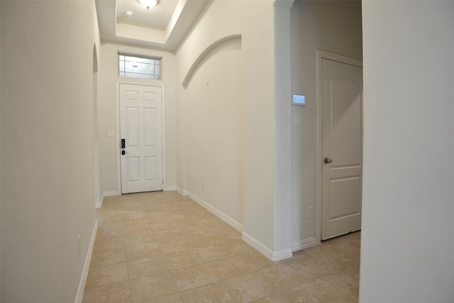 hall featuring a tray ceiling and light tile patterned floors