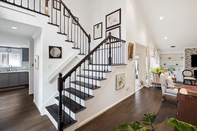 stairway featuring a stone fireplace, sink, hardwood / wood-style flooring, built in shelves, and a towering ceiling