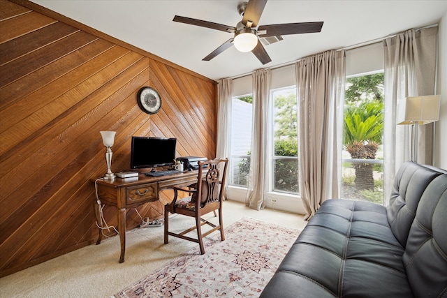 home office featuring light colored carpet, ceiling fan, and wooden walls