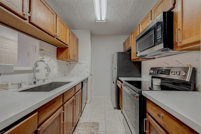 kitchen with appliances with stainless steel finishes, tasteful backsplash, a textured ceiling, sink, and light tile patterned floors