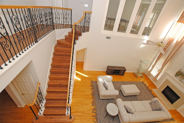 living room featuring hardwood / wood-style floors, ceiling fan, a high ceiling, and a tiled fireplace