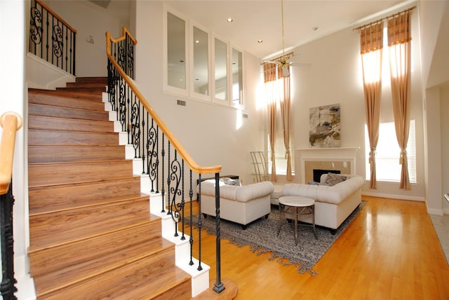 living room with ceiling fan, a towering ceiling, and hardwood / wood-style flooring