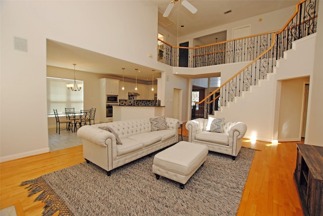 living room featuring a high ceiling, ceiling fan with notable chandelier, hardwood / wood-style flooring, and plenty of natural light