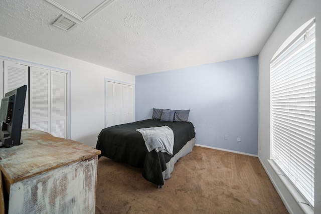 carpeted bedroom featuring a textured ceiling and two closets