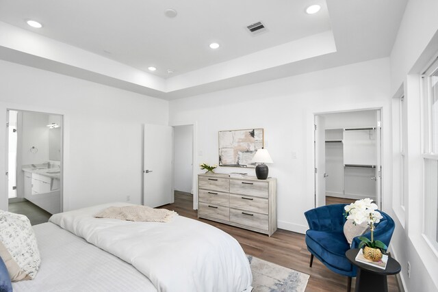 bedroom with ensuite bathroom, a raised ceiling, dark hardwood / wood-style floors, a spacious closet, and a closet